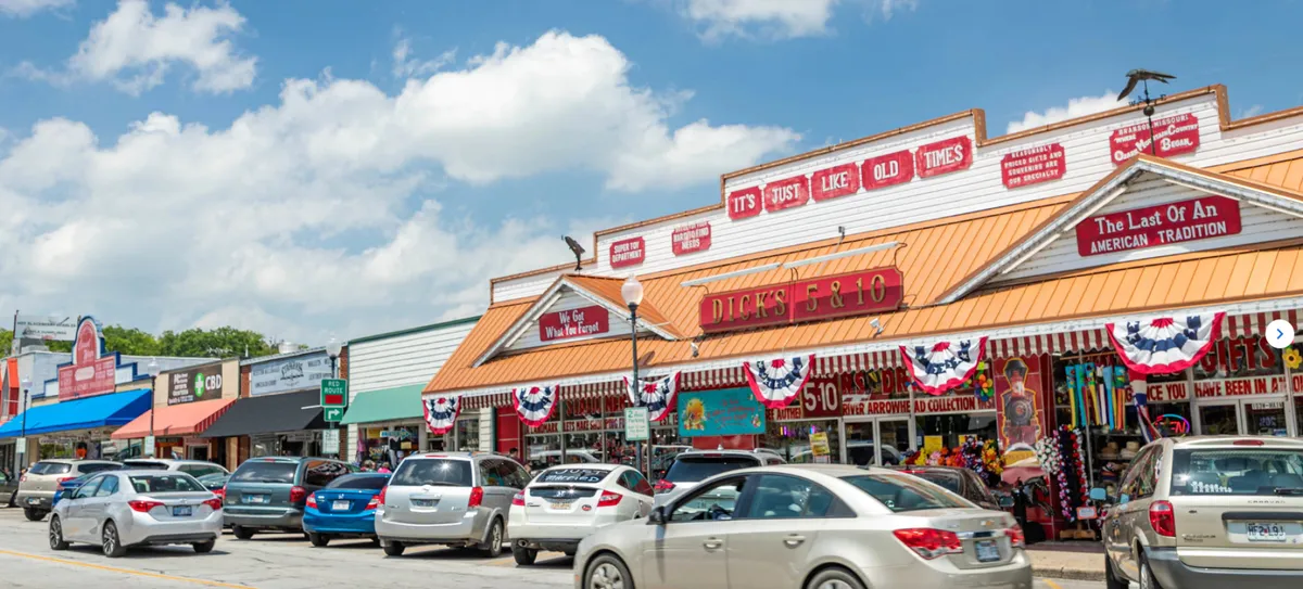 This image depicts colorful storefronts along a street decorated with banners and bustling with parked cars, highlighting the festive and lively atmosphere just outside the park. It suggests the excitement continues beyond the rides, with opportunities for shopping, dining, and festival fun.