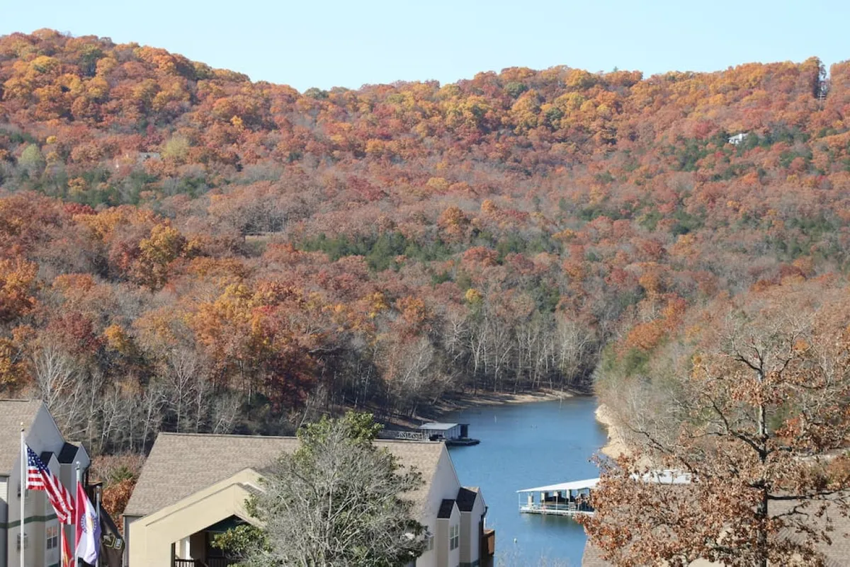 A tranquil view of Table Rock Lake framed by vibrant autumn trees and a charming boathouse, capturing the serene beauty of the waterfront. The colorful foliage reflects on the calm water, illustrating the changing seasons.