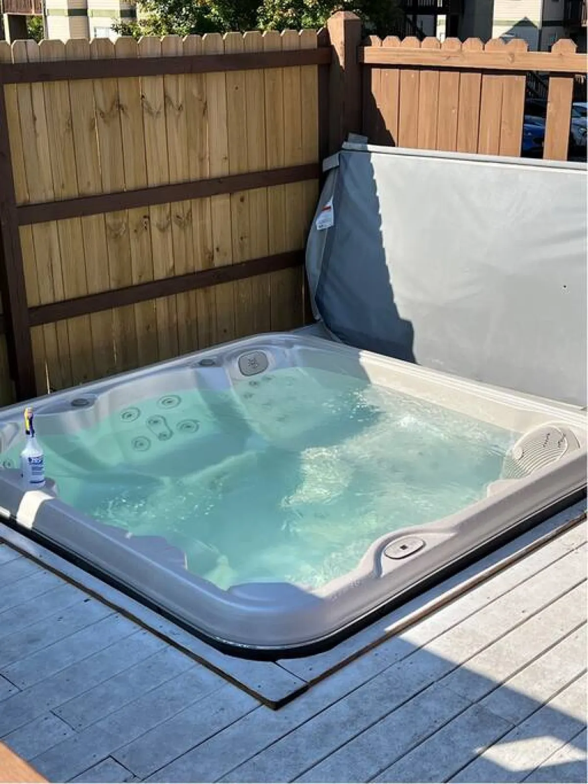 This exterior image features a hot tub set on a wooden deck, bordered by a wooden fence for privacy, with ample decking space for relaxation and socializing. The setting is tranquil and inviting, emphasizing both leisure and outdoor enjoyment.