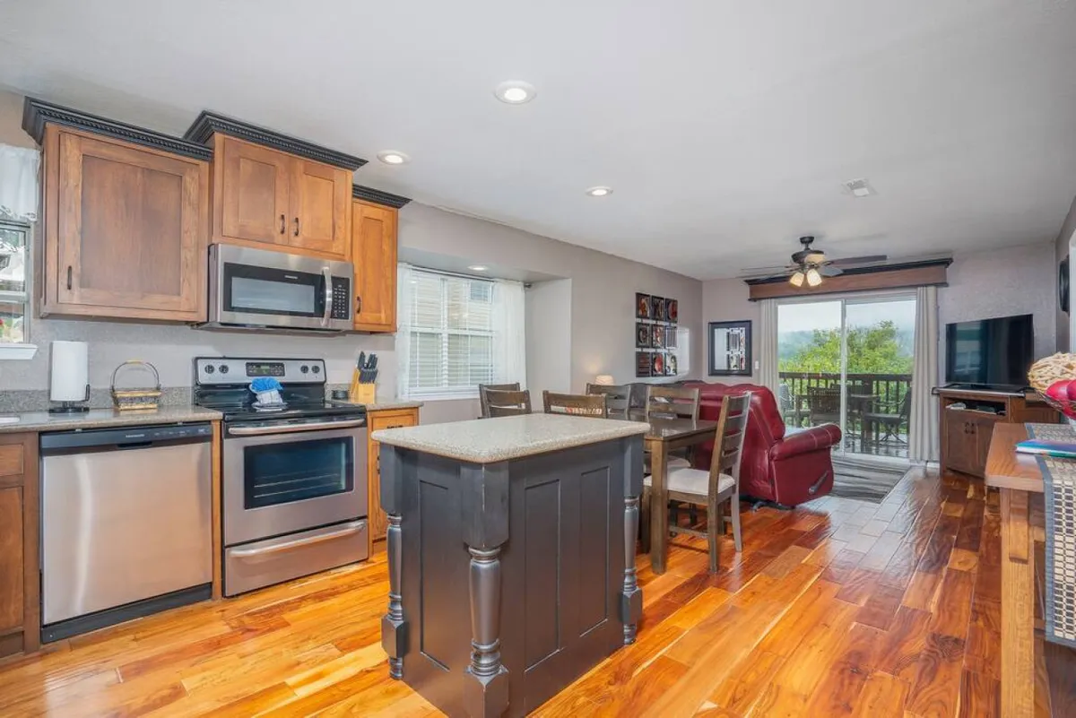 A wide interior view that includes a kitchen island, dining area, window with a view, and the living area. The space is open and airy, with plenty of room for socializing, dining, and relaxing—an ideal backdrop for family celebrations and shared experiences.