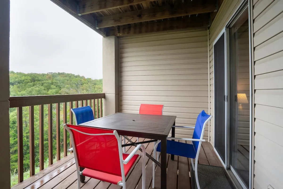 An exterior scene showcasing an outdoor dining table surrounded by colorful chairs and a lush green landscape. The mood is relaxed and social, suggesting a vibrant community space for gathering, playing, or unwinding together.