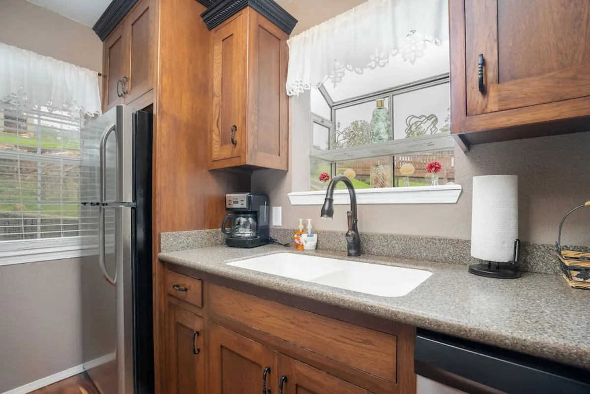 A close-up view of a granite kitchen countertop with a modern stainless steel refrigerator, window decorated with small accents, and a sleek faucet. The cozy setup is perfect for baking, socializing, or enjoying a quiet morning coffee.