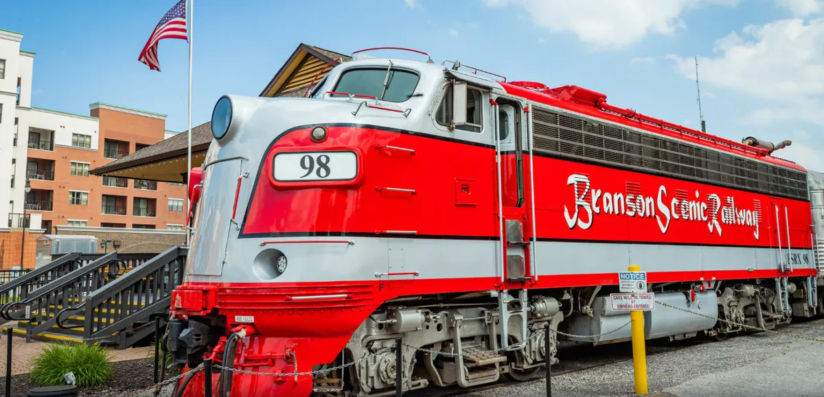 A vintage train, draped with an American flag, is stationed beside charming buildings, evoking the sense of discovery and adventure that awaits visitors to Silver Dollar City. The train ride is both an iconic park feature and a symbol of the journey families will take together.