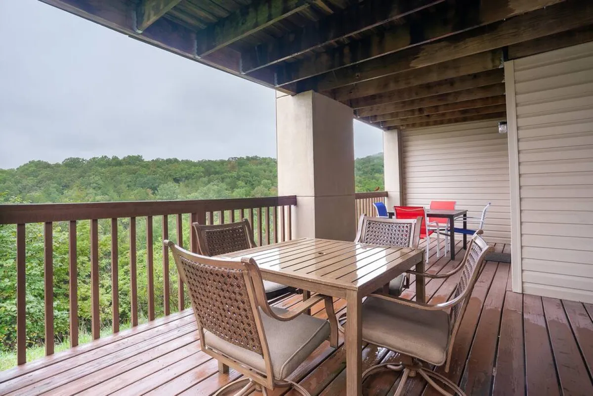 This exterior image highlights a wooden dining table with woven chairs set on a patio, overlooking a green landscape. The setting is peaceful and ideal for outdoor relaxation or enjoying a meal after recreational activities.