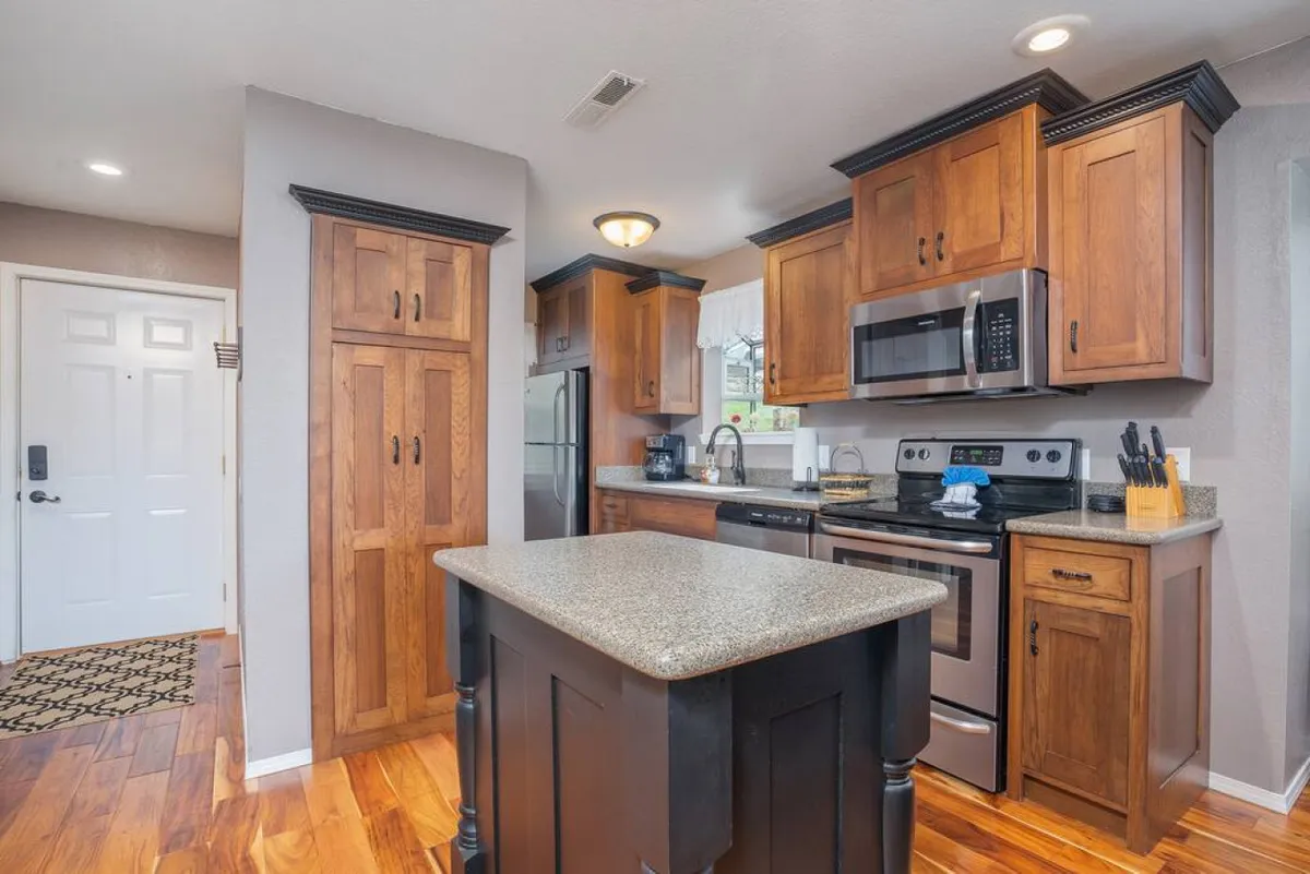 A spacious and modern kitchen featuring a prominent kitchen island, stainless steel appliances, and warm wood cabinetry. The layout includes generous counter space and seating areas ideal for cooking and entertaining. Natural light fills the room, enhancing its inviting atmosphere.