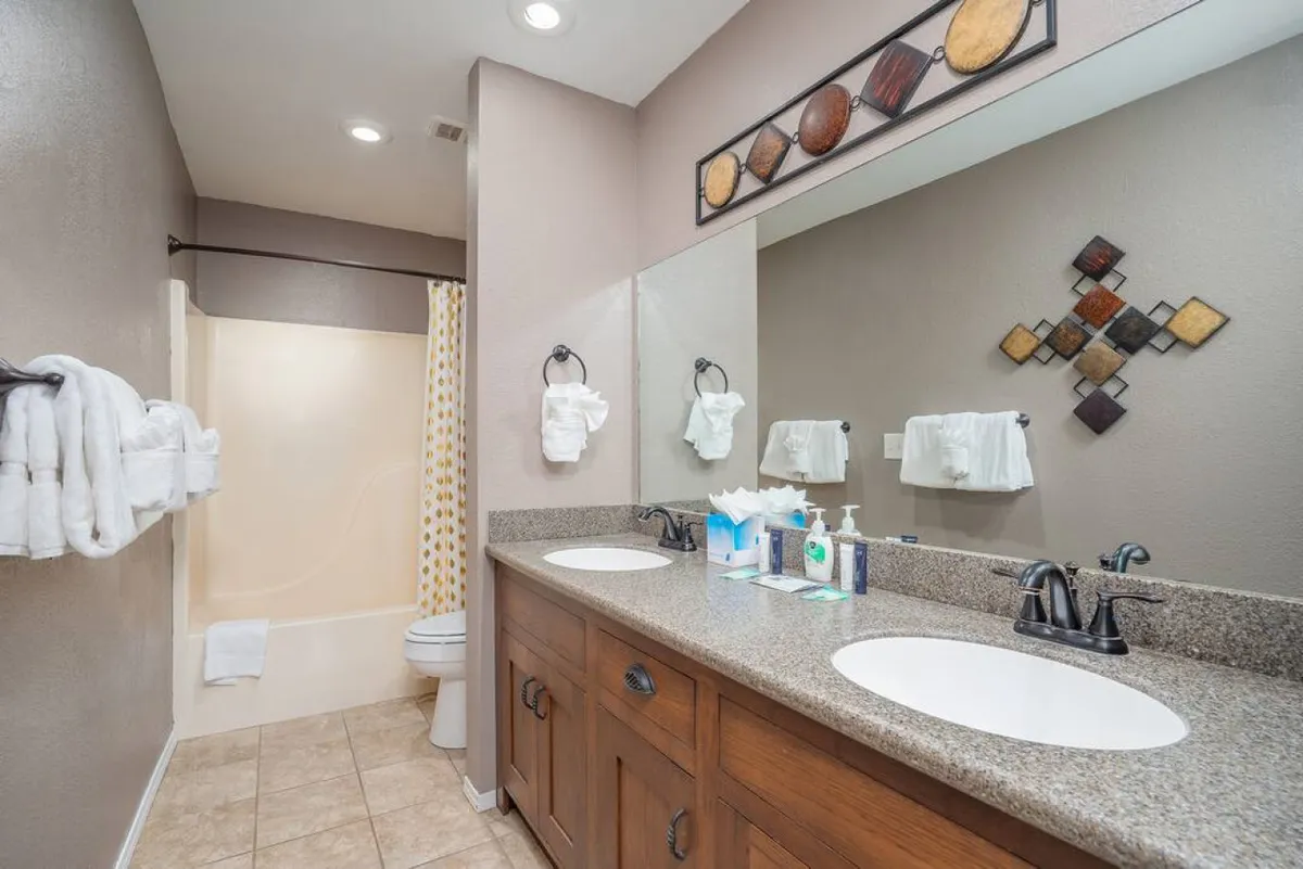 A modern bathroom with double vanity sinks, decorative wall art, and a bathtub with a curtain. The space feels calm and peaceful, inviting guests to enjoy a relaxing bath or morning routine.